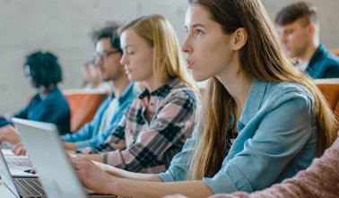 Zwei junge Frauen und drei junge Männer sitzen mit Laptops in einem Hörsaal. 